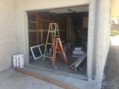 Open garage under renovation with ladders, lumber, and a window frame inside