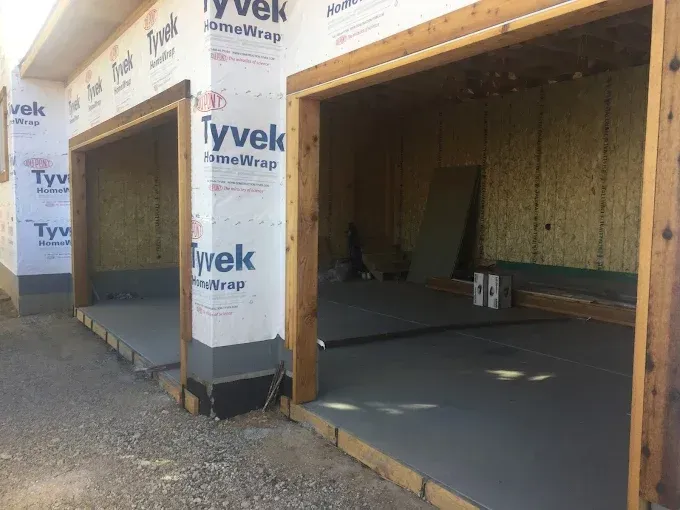 Two open garage bays under construction with Tyvek wrap and unfinished wooden framing