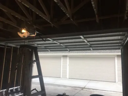 Dim garage interior with a ladder and open garage door showing a bright driveway and closed white doors outside