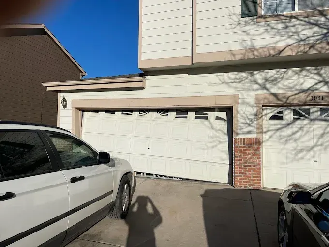 Damaged garage door with dents and bent panels, framed by parked cars in a suburban driveway