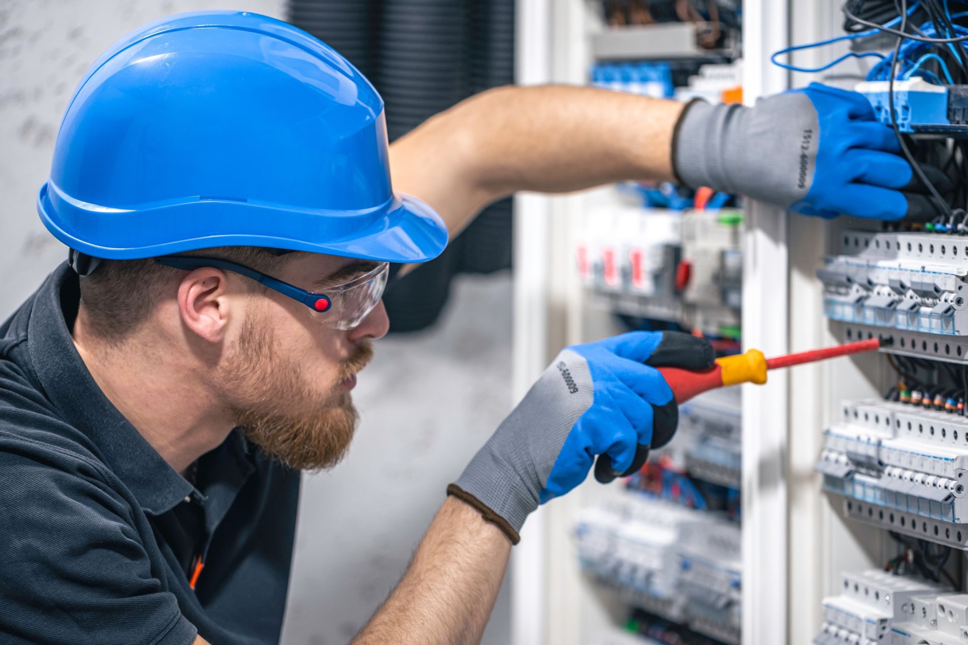 A man wearing a hard hat and gloves is working on an electrical panel.