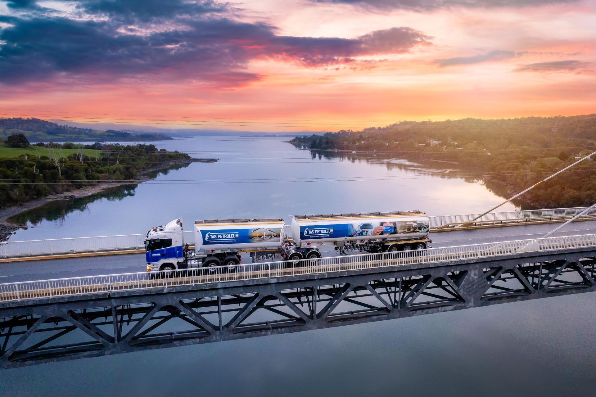 An aerial view of a truck driving on a bridge over a river.