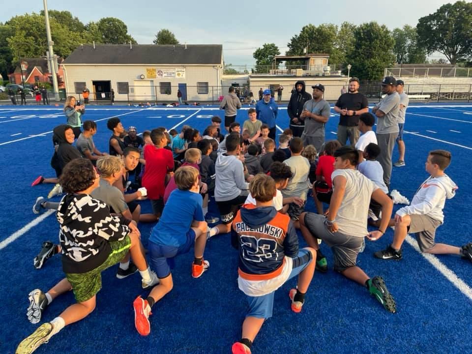 Youth football team on a blue field, listening to coaches.