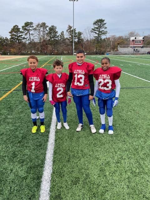 Four young football players in red and blue uniforms stand on a green field.