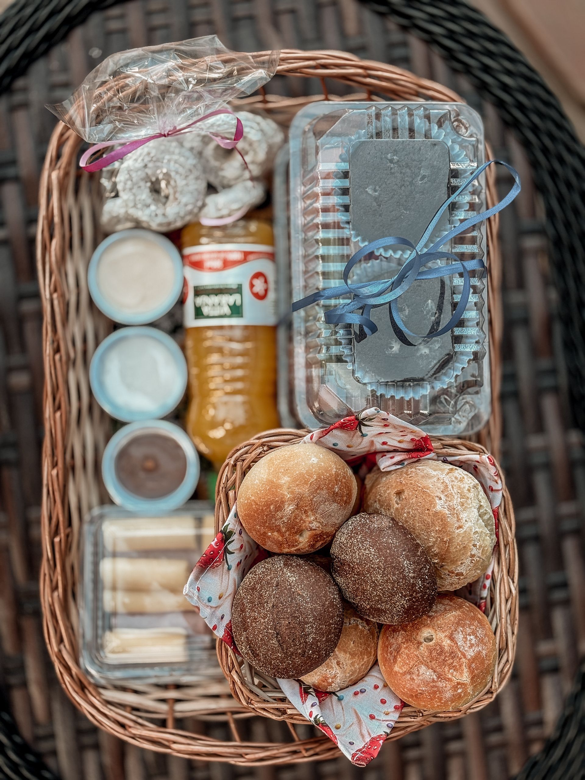 Cesta de piquenique recheada de comida: doces, pães, suco, molhos e uma sobremesa.
