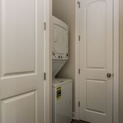 Stacked washer and dryer in a narrow closet with two white doors.