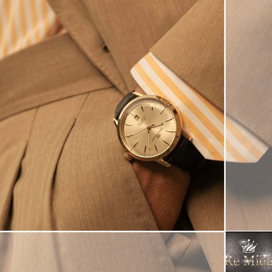 Uomo in abito marrone chiaro con orologio d'oro e polsino a strisce gialle in vista.