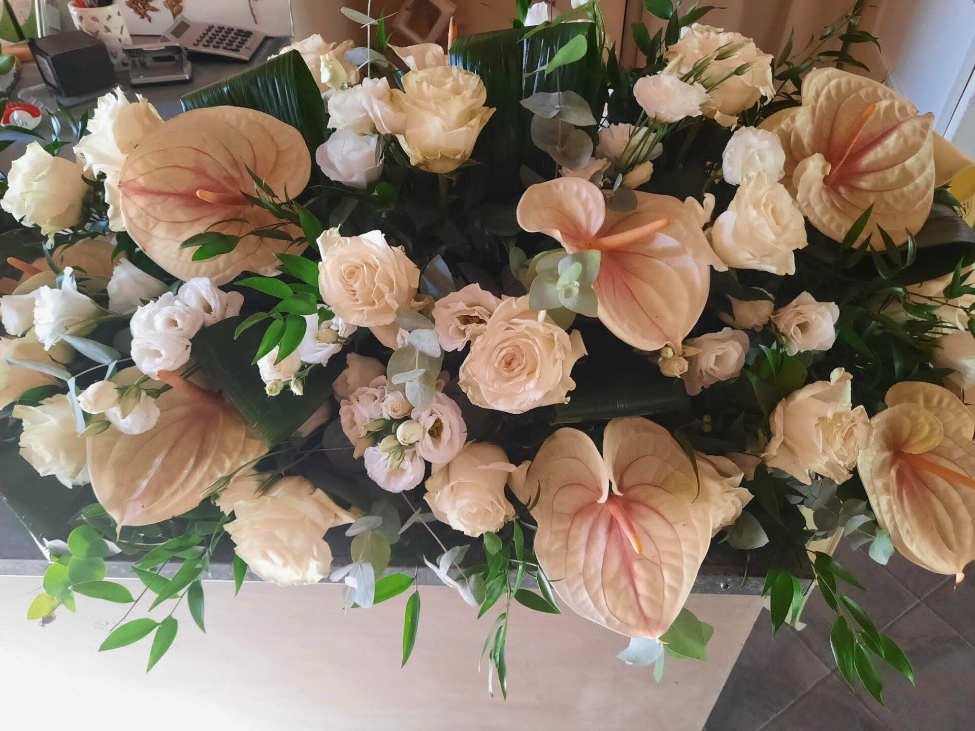 Composizione floreale color pesca e crema con rose e anthurium su un centrotavola scuro.