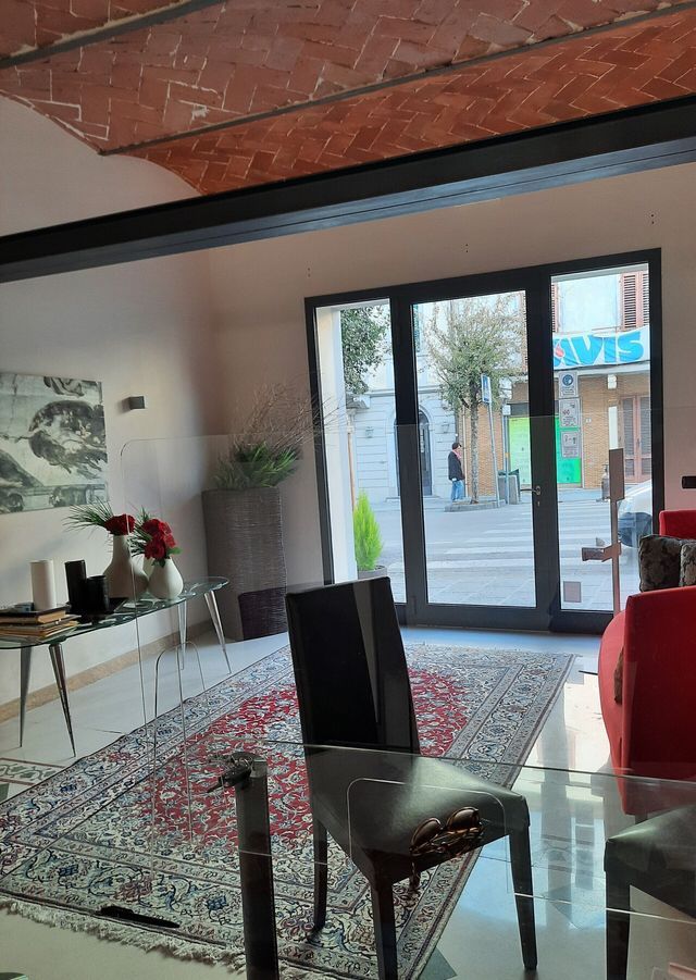 Stanza moderna con porte a vetri, tappeto a motivi geometrici, sedie e un divano rosso che si affaccia sulla strada.