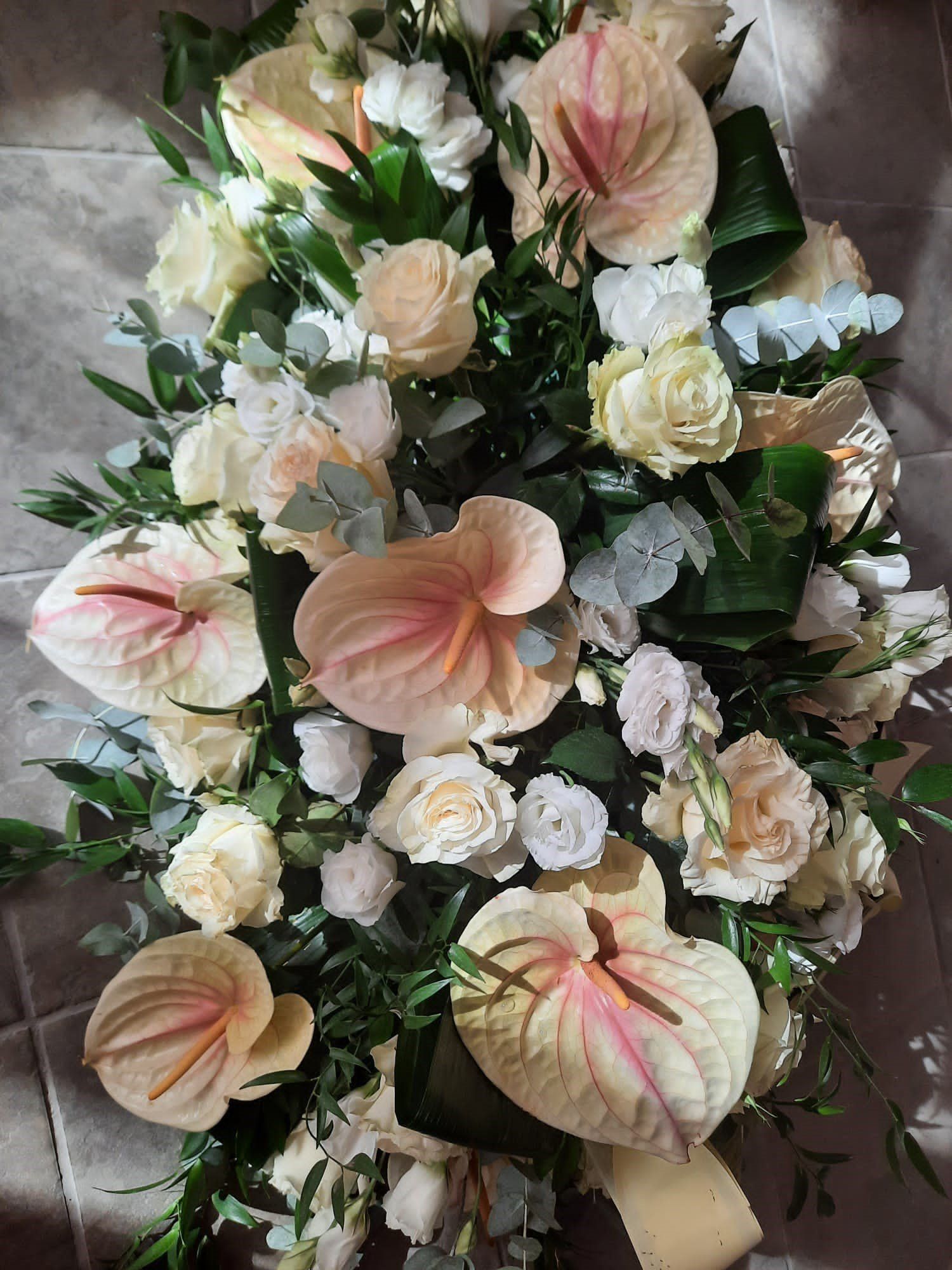 Ghirlanda floreale dai toni pastello con fiori color pesca, bianchi e crema e foglie verdi.