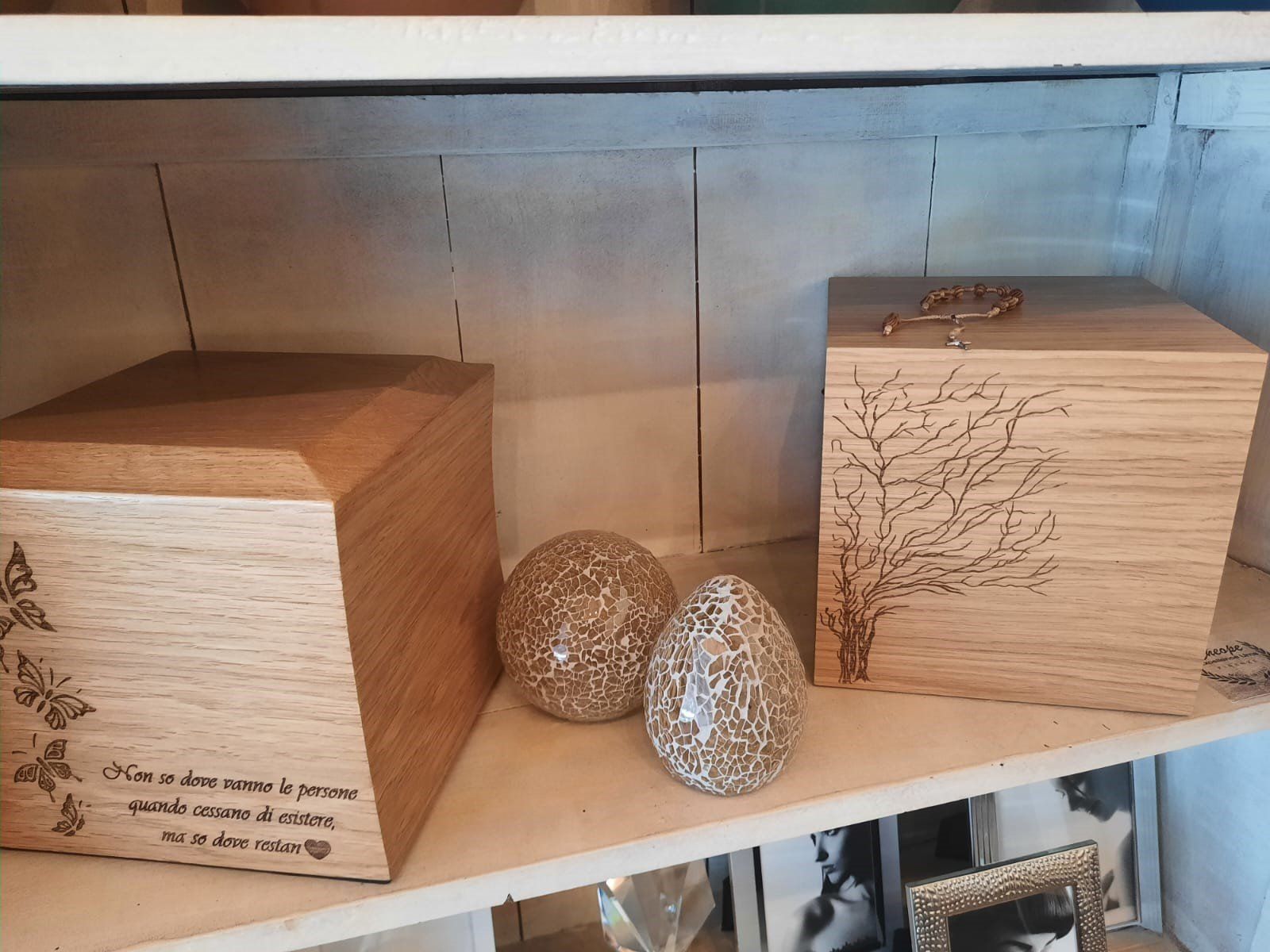 Due scatole decorative in legno e due uova intrecciate su una mensola bianca contro una parete chiara