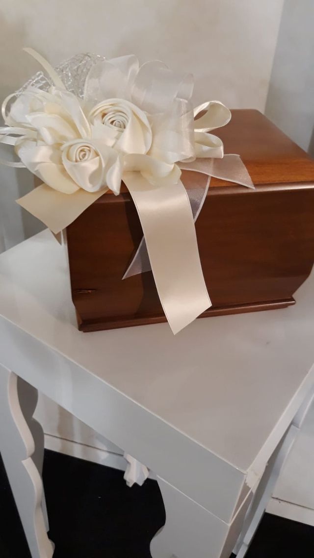 Un fiocco regalo floreale bianco su una piccola scatola di legno marrone, appoggiata su un tavolo bianco.