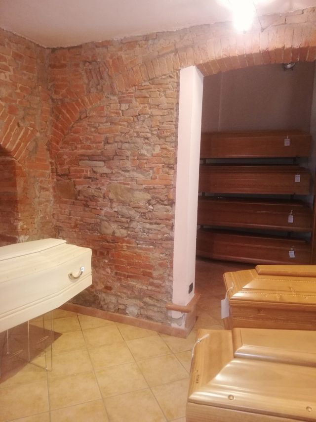 Seminterrato con pareti in mattoni, scale, pavimento piastrellato e panche di legno in una piccola stanza.