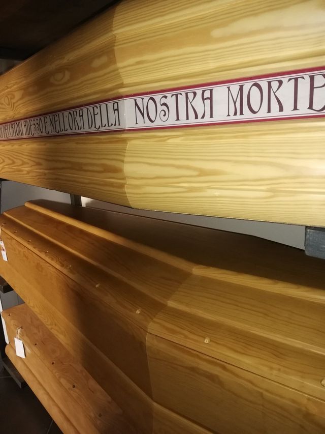 Coperchi di bare di legno in fila, uno con testo latino intagliato su una fascia rosa