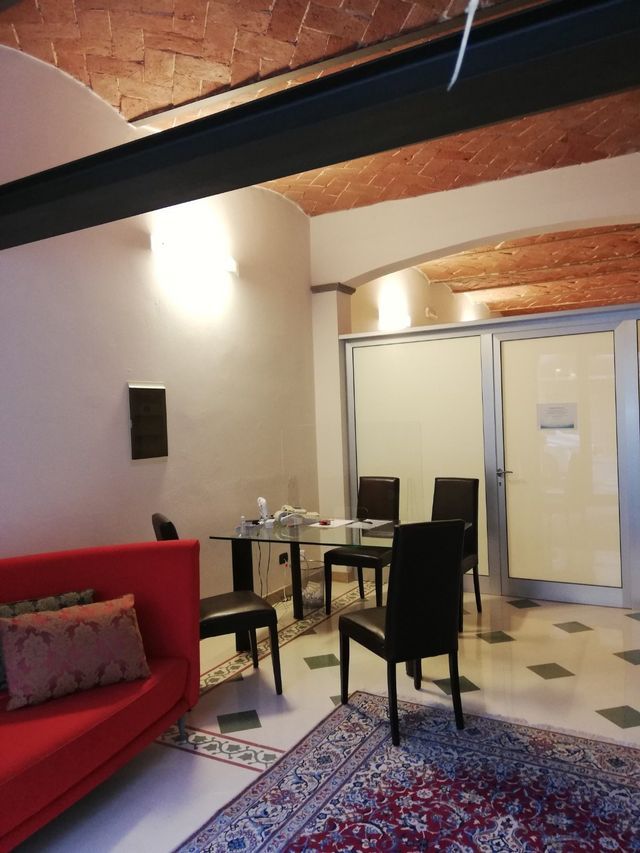 Soggiorno moderno con divano rosso, tavolo da pranzo, sedie nere, tappeto a motivi geometrici e porte a vetri sotto travi a vista.