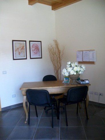 Piccola area riunioni in ufficio con tavolo in legno, sedie nere, quadri alle pareti, fiori e bacheca.