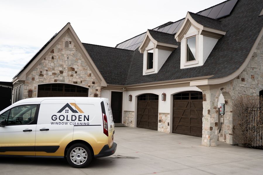 Golden service van parked outside a stone house with a dark roof and garage doors