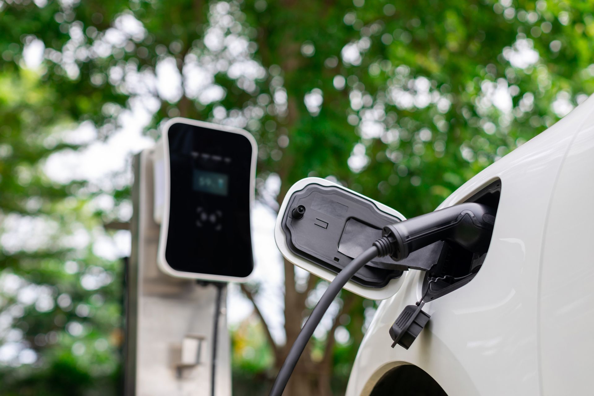 Electric car charging at a public station with a cable plugged into the white vehicle.