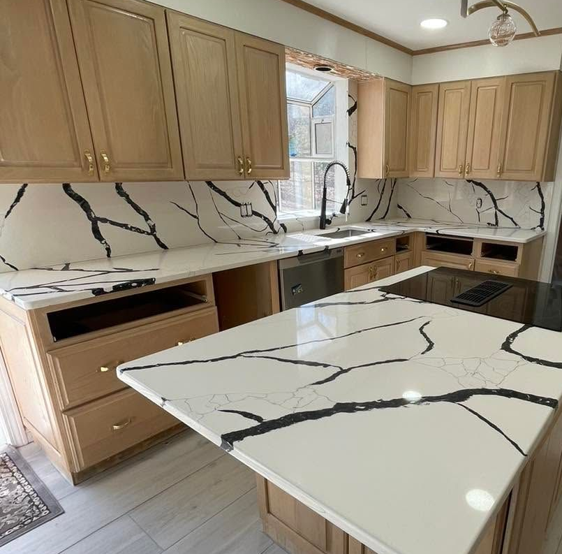 Modern kitchen with light wood cabinets, white marble-look counters, and a large island with black veining.