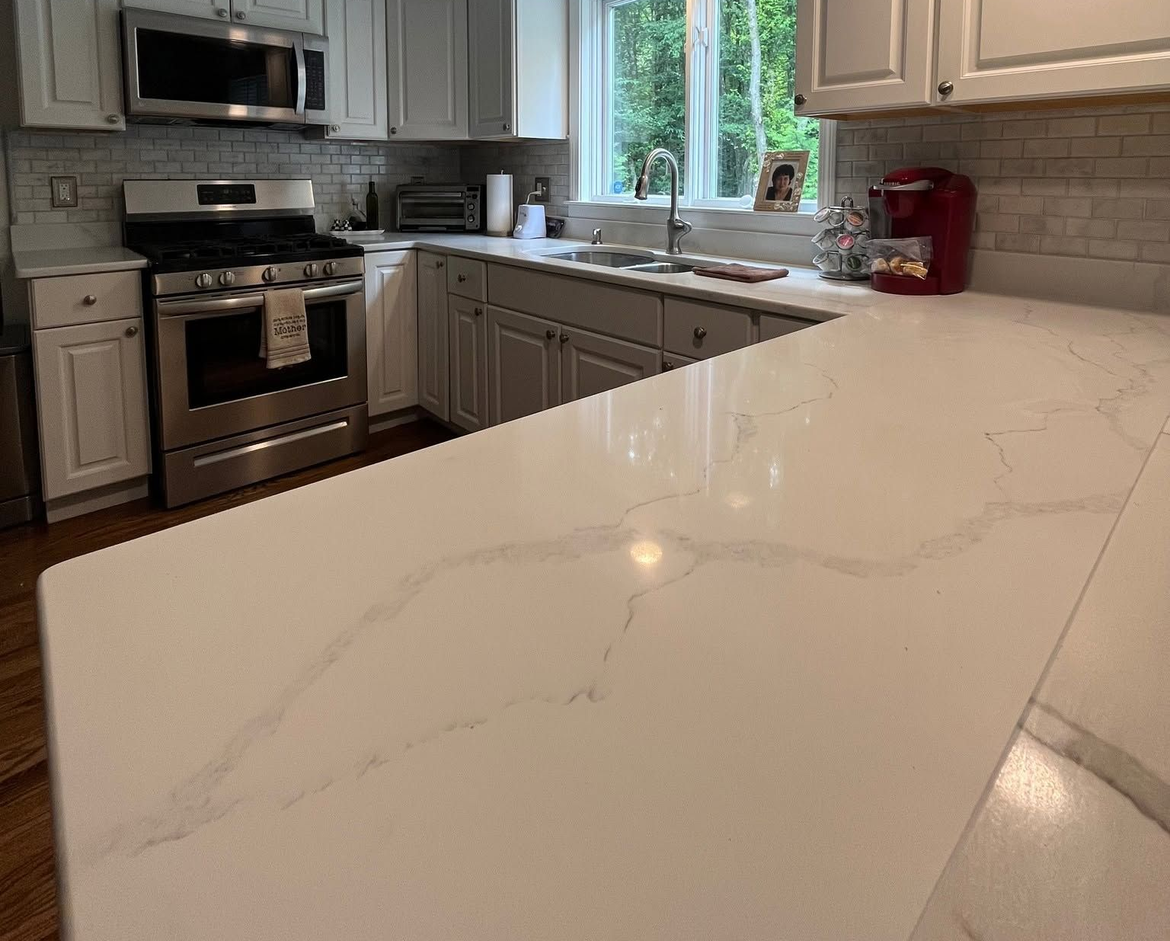 Modern kitchen with white marble countertop, stainless steel appliances, gray cabinets, and window over the sink