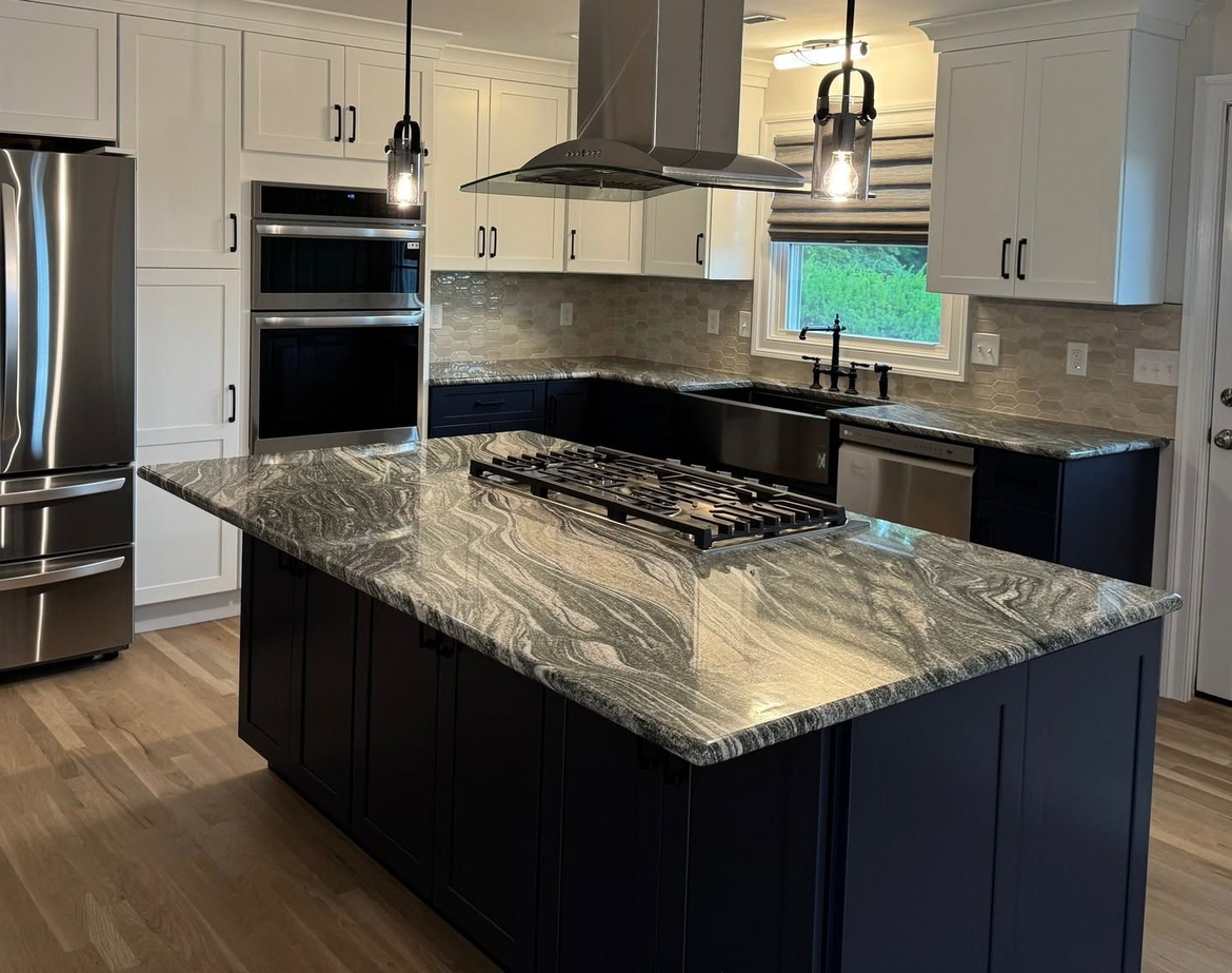 Modern kitchen with large granite island, white cabinets, stainless steel appliances, and pendant lights.