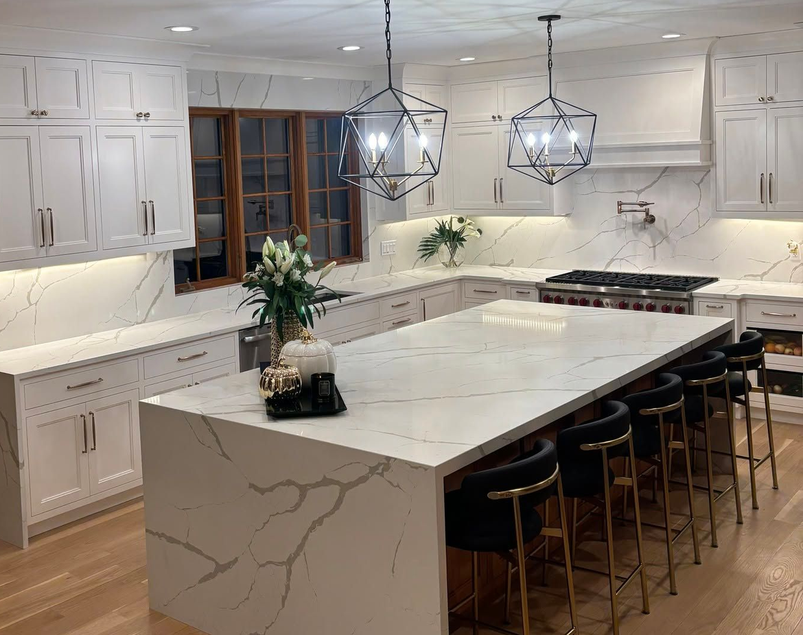 Bright modern kitchen with white cabinets, marble island, pendant lights, and bar stools