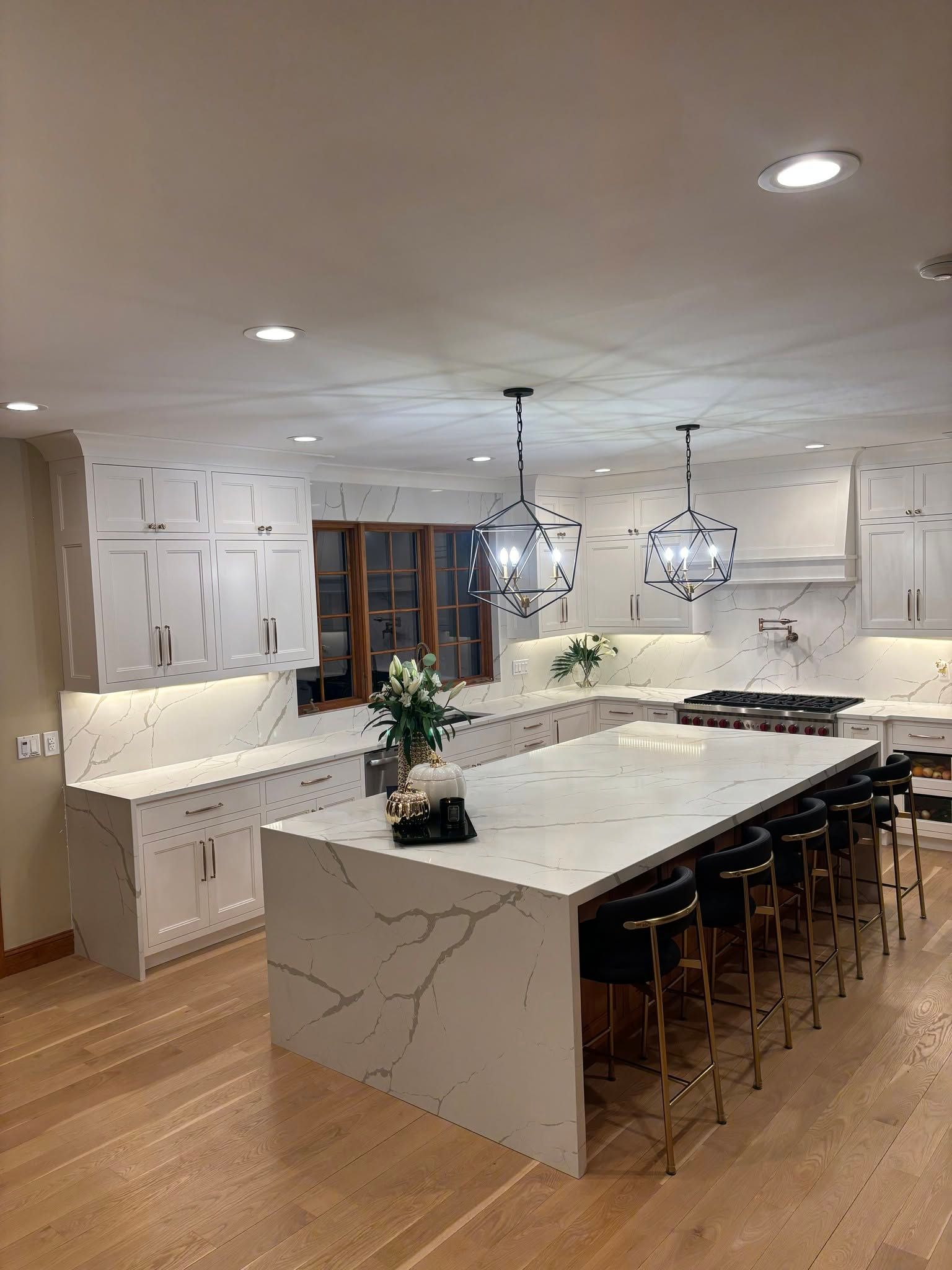 Modern kitchen with a large marble island, bar stools, pendant lights, and warm wood flooring.