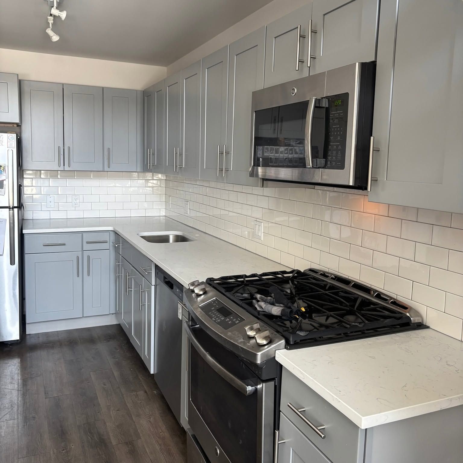 Modern gray kitchen with white countertops, subway tile backsplash, and stainless steel appliances.