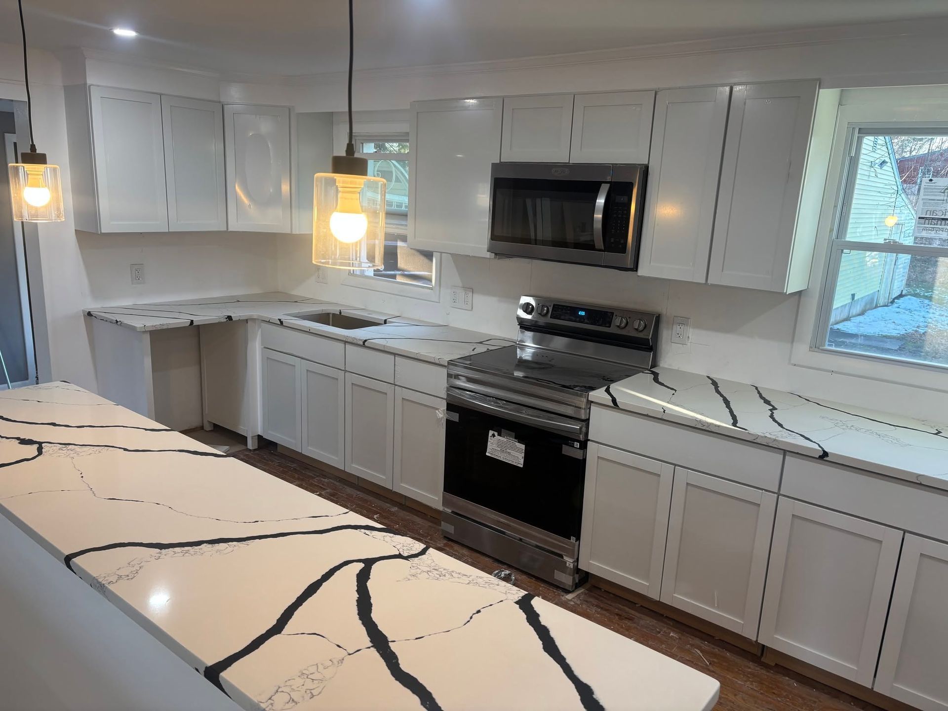 Modern white kitchen with black-veined marble island, white cabinets, stainless steel stove, and pendant lights