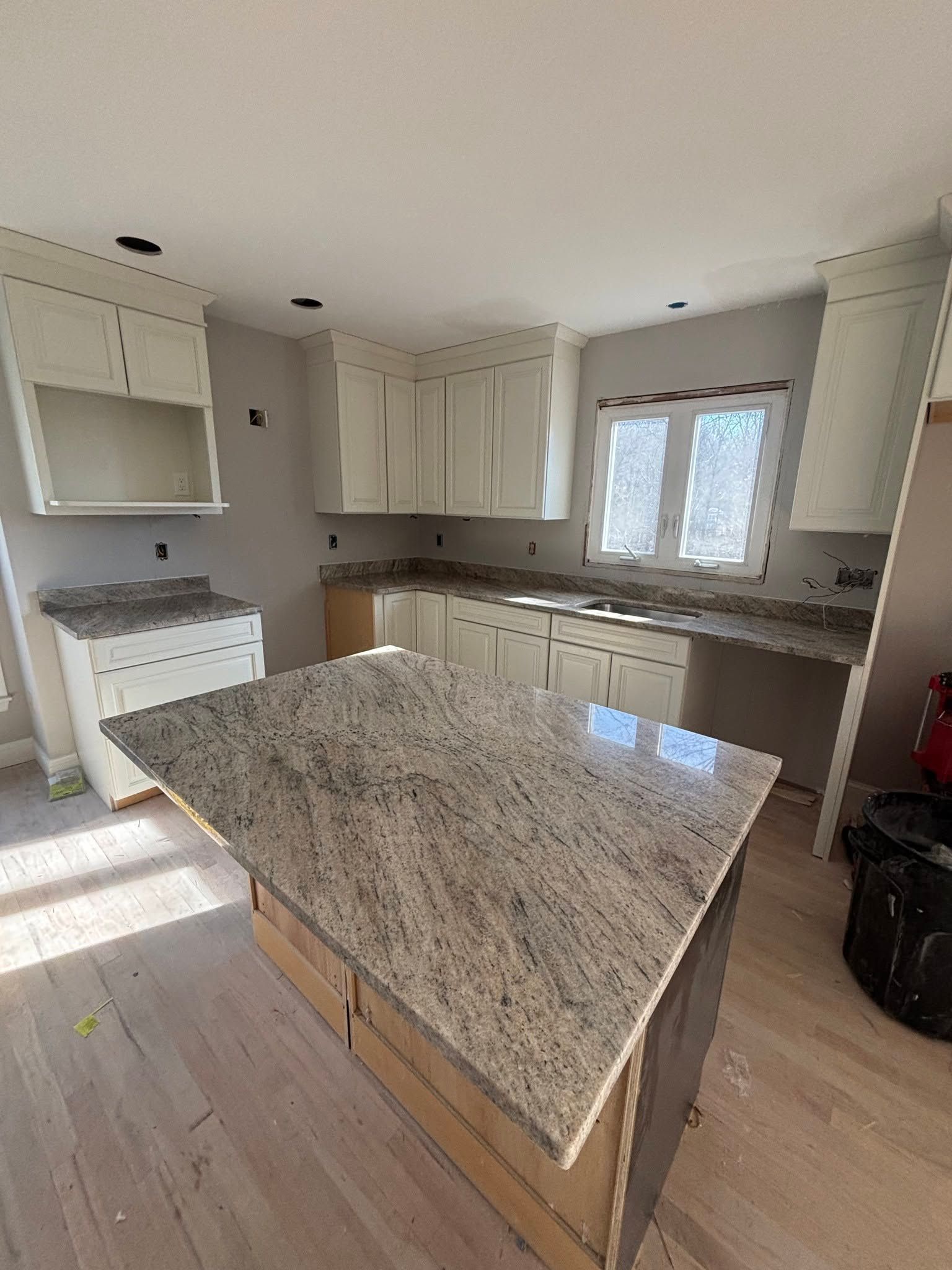 Bright kitchen with white cabinets, granite island, and window over the sink