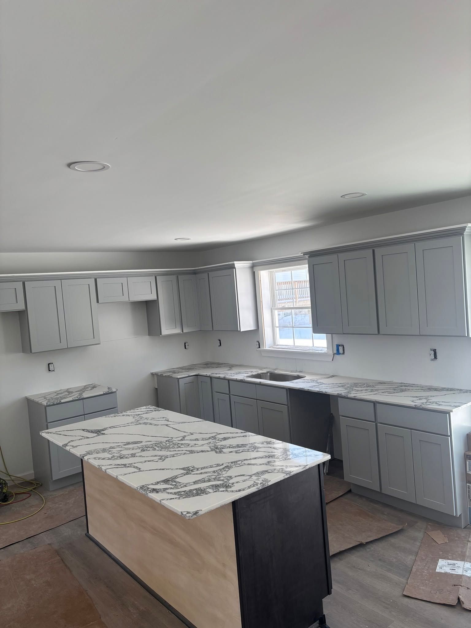 Kitchen with gray cabinets, white countertops, and an island in a bright, unfinished room.