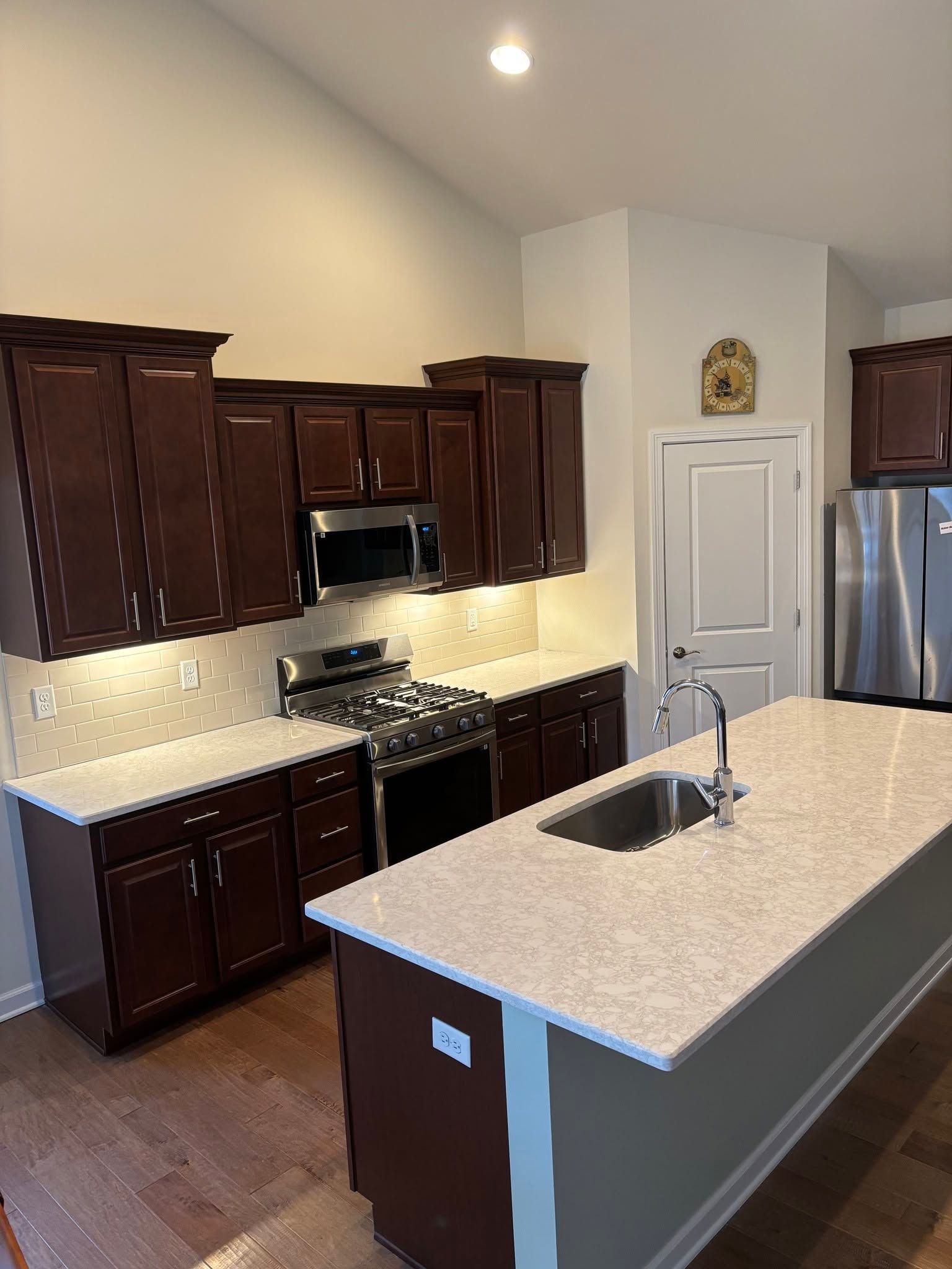 Modern kitchen with dark wood cabinets, granite island, stainless appliances, and hardwood floors