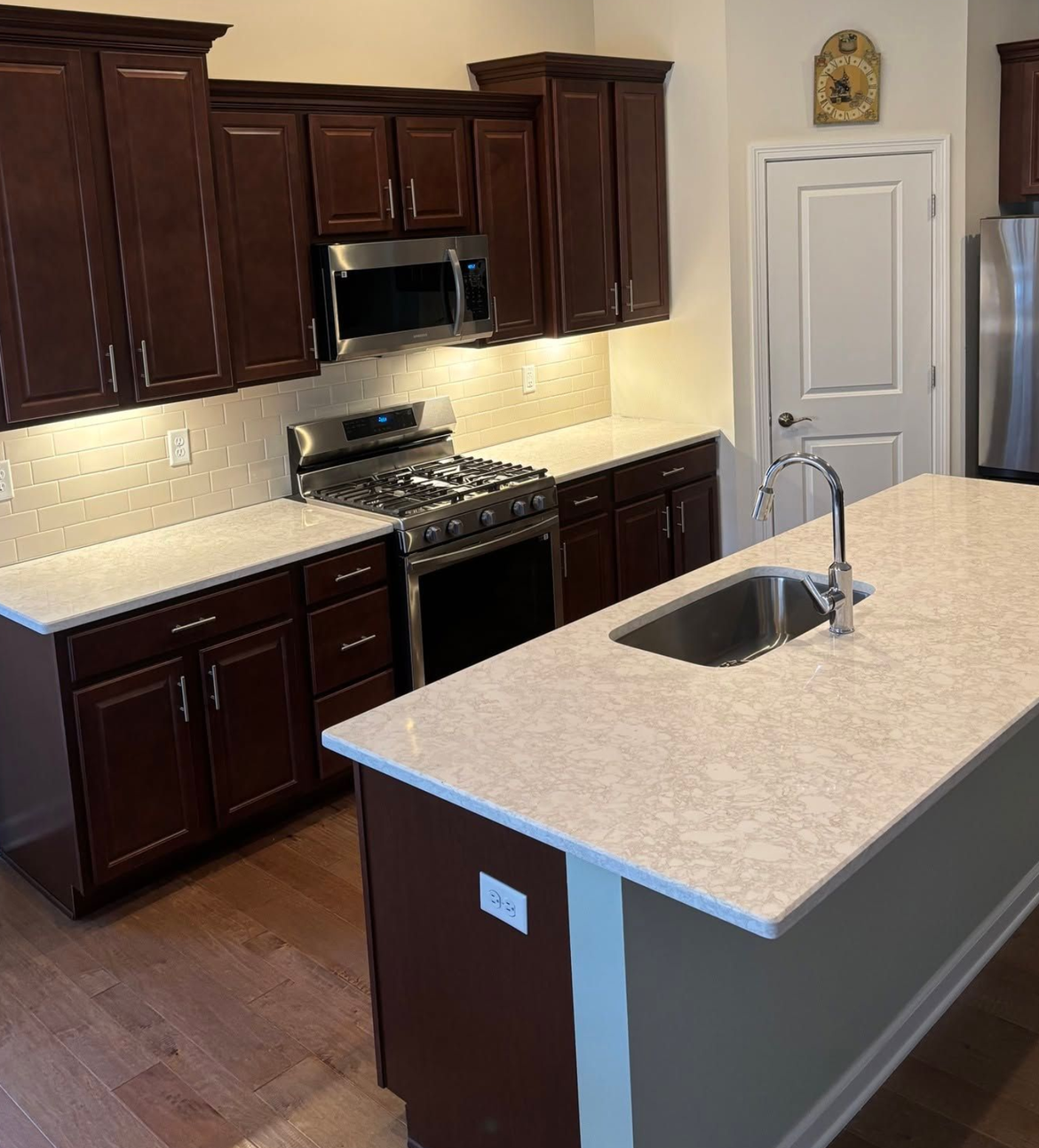 Modern kitchen with dark wood cabinets, stainless appliances, and a light stone island with sink.