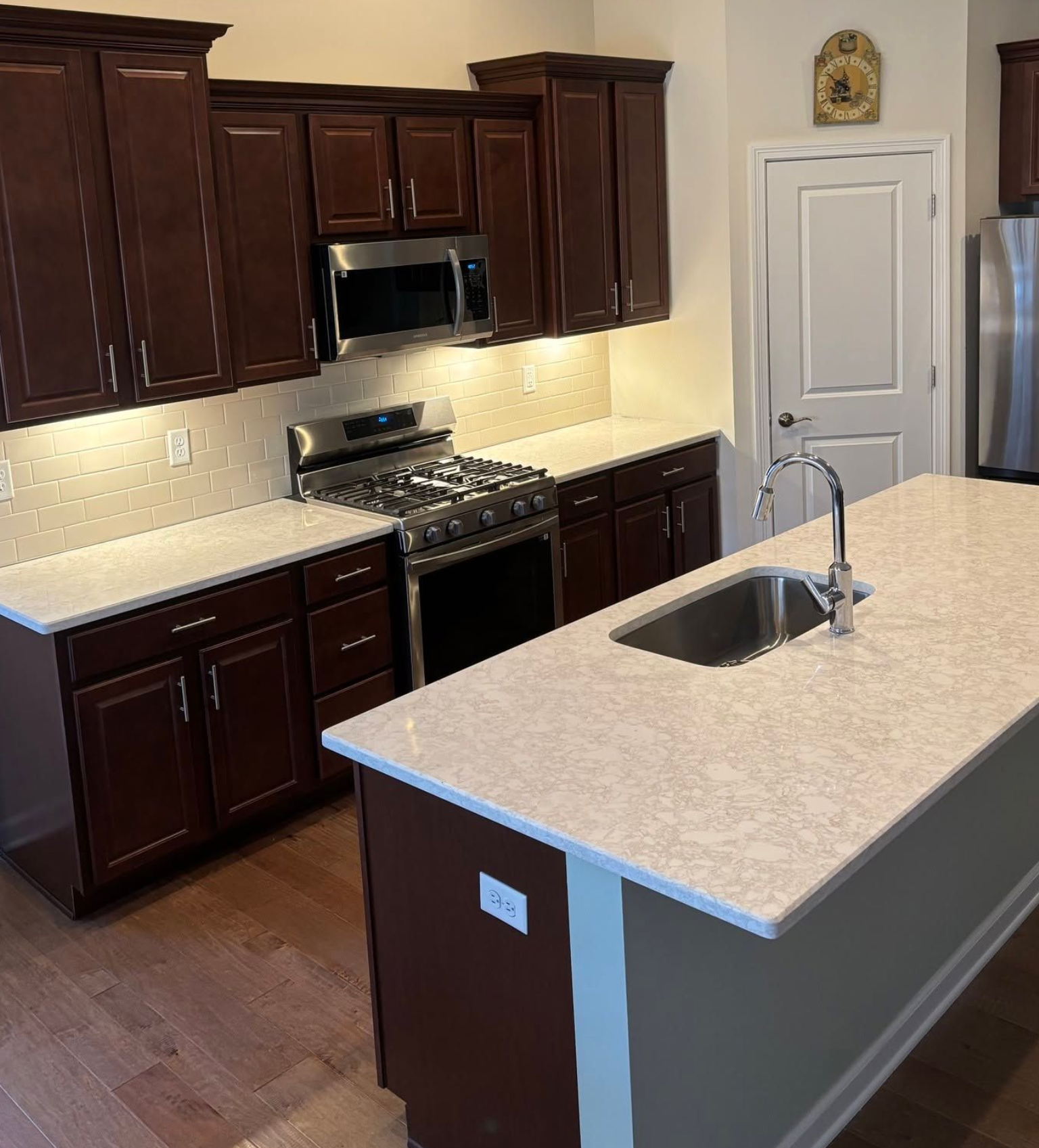 Modern kitchen with dark wood cabinets, stainless appliances, and a light stone island with sink.