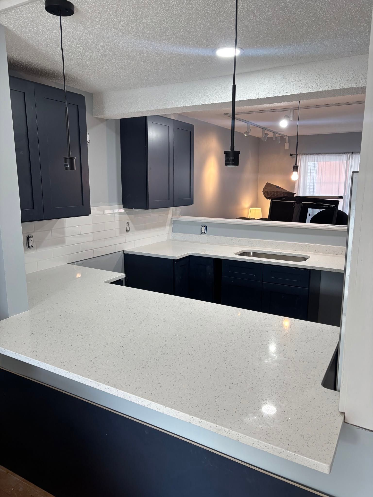 Modern kitchen with white quartz island, dark cabinets, and pendant lights in an open-concept space