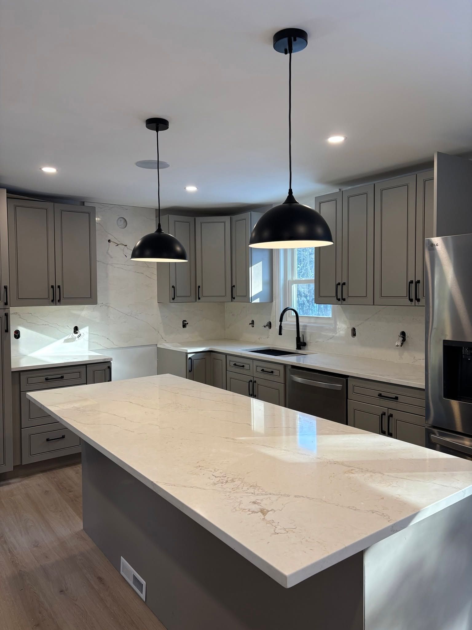 Modern kitchen with large white island, black pendant lights, light cabinets, and stainless steel appliances
