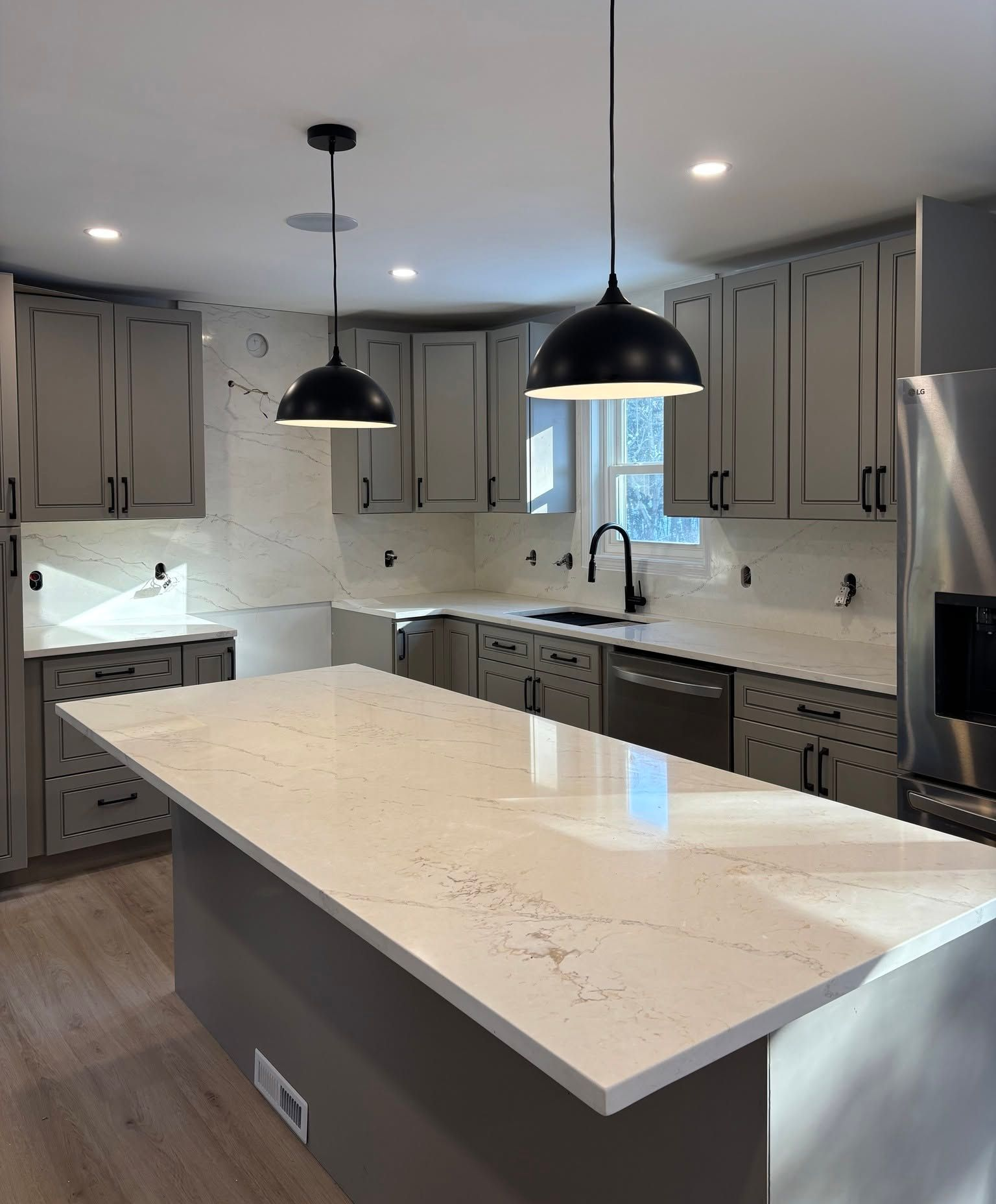 Modern kitchen with gray cabinets, marble island, white countertops, and black pendant lights