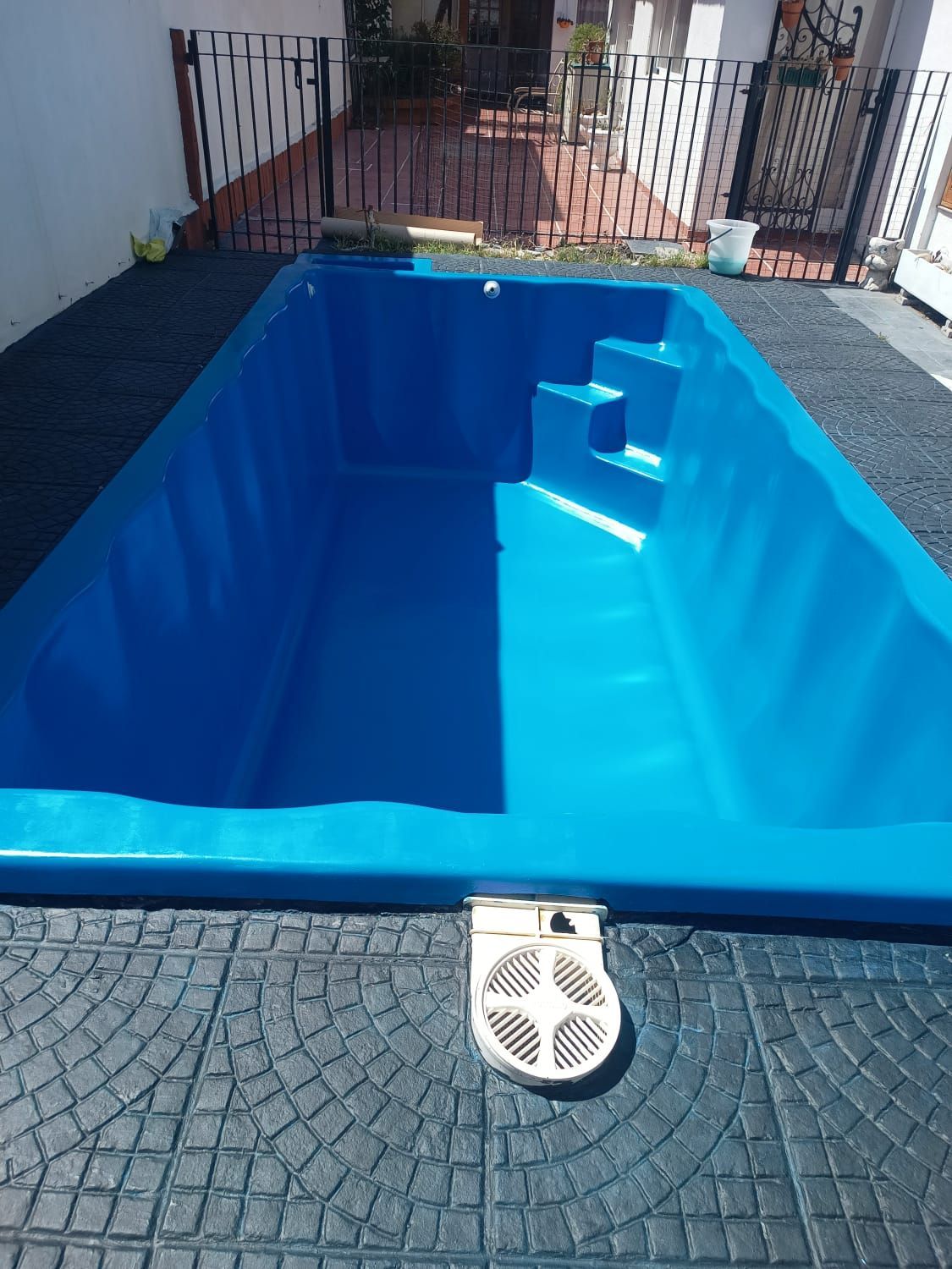 Piscina rectangular de color azul con escalones, rodeada de baldosas de piedra gris.
