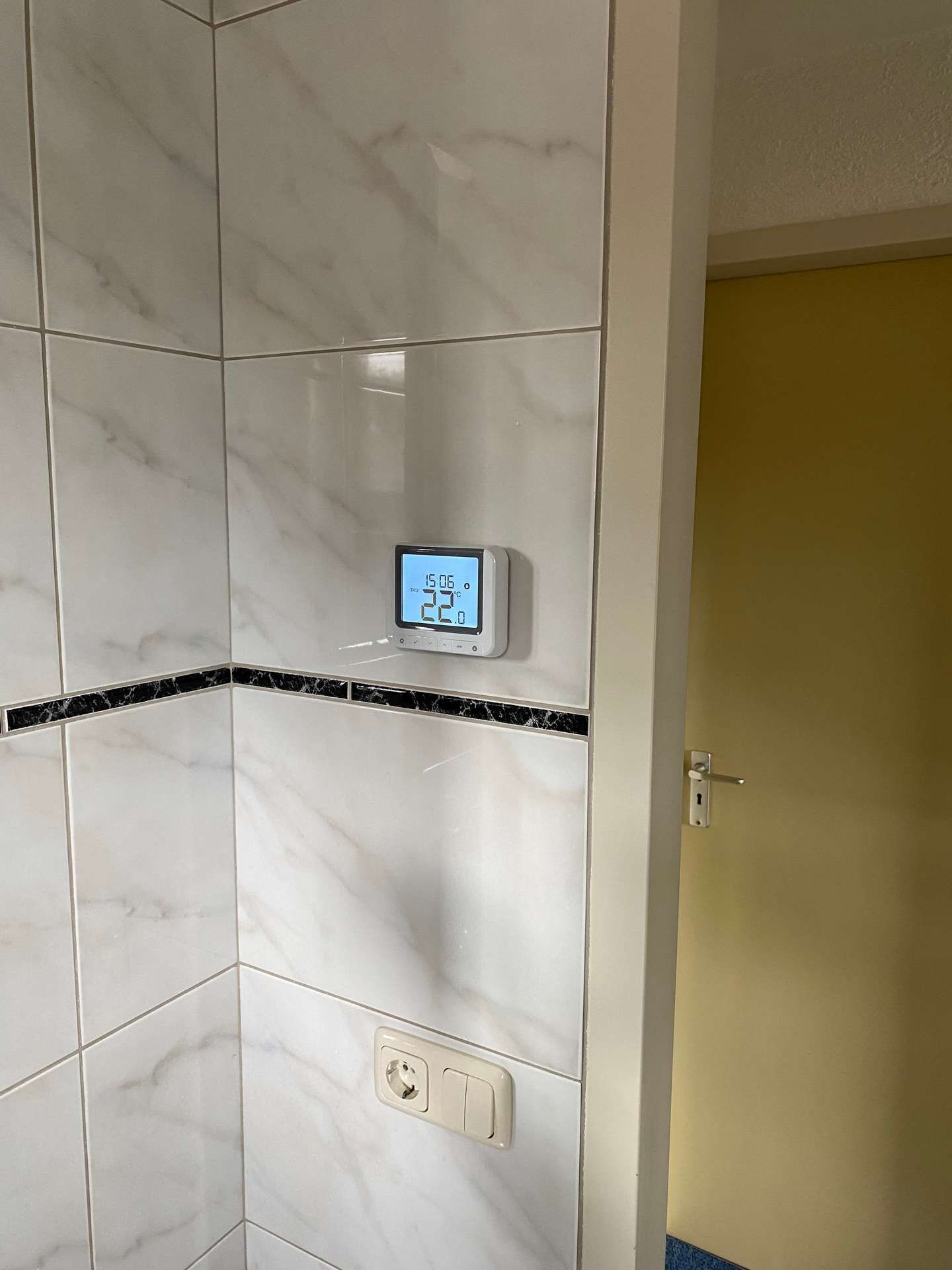 In een badkamer wordt een thermostaat op een betegelde wand gemonteerd.