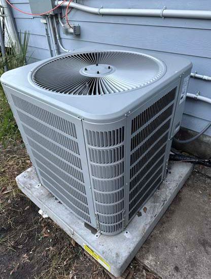 A large air conditioner is sitting on top of a concrete platform outside of a house.