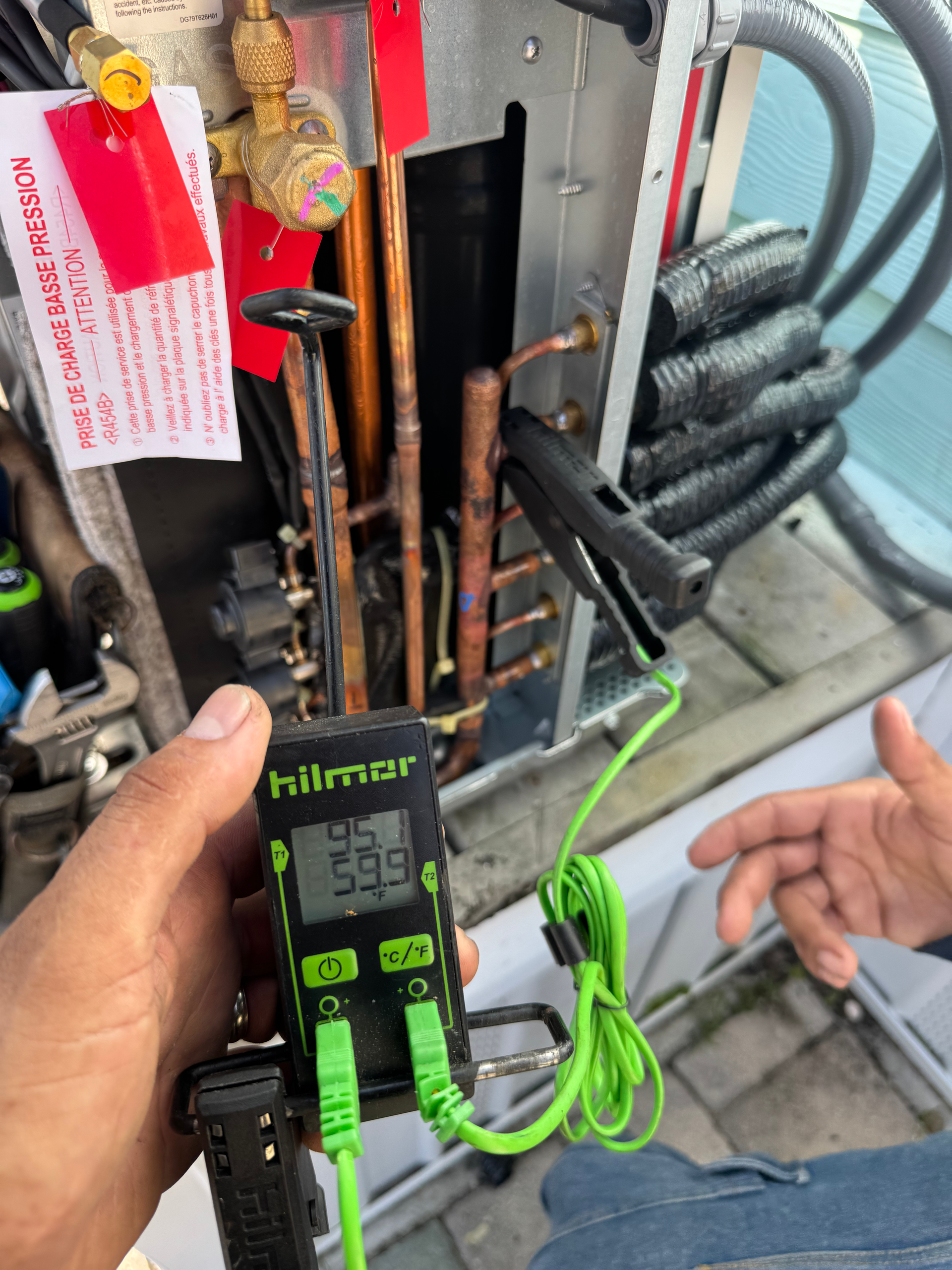 A person using a temperature reader on AC unit's copper pipes outdoors. Display reads 59.5Β°F.
