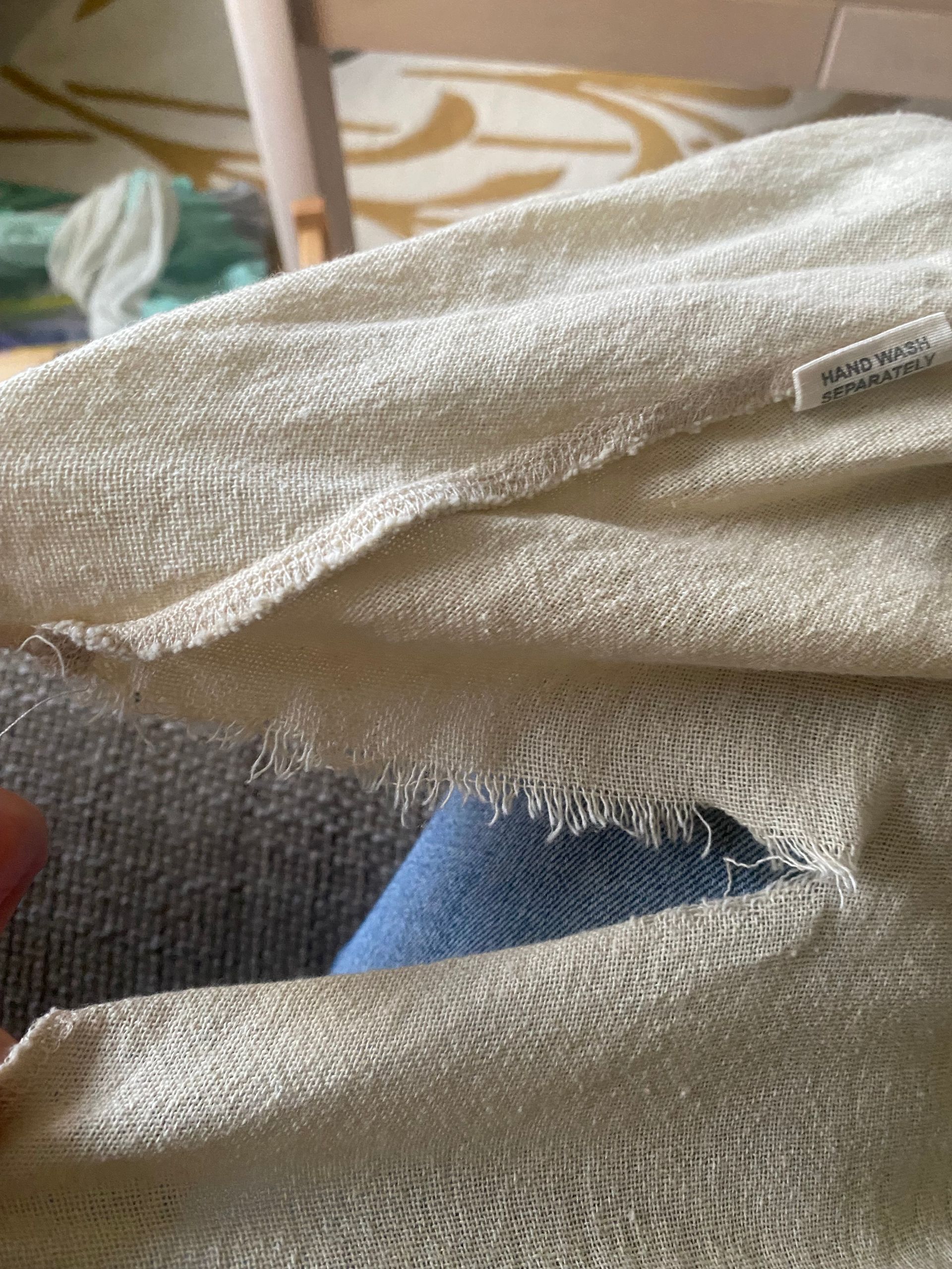 Close-up van crèmekleurige gebreide stof met een gat, waardoor de denimstof eronder zichtbaar is.