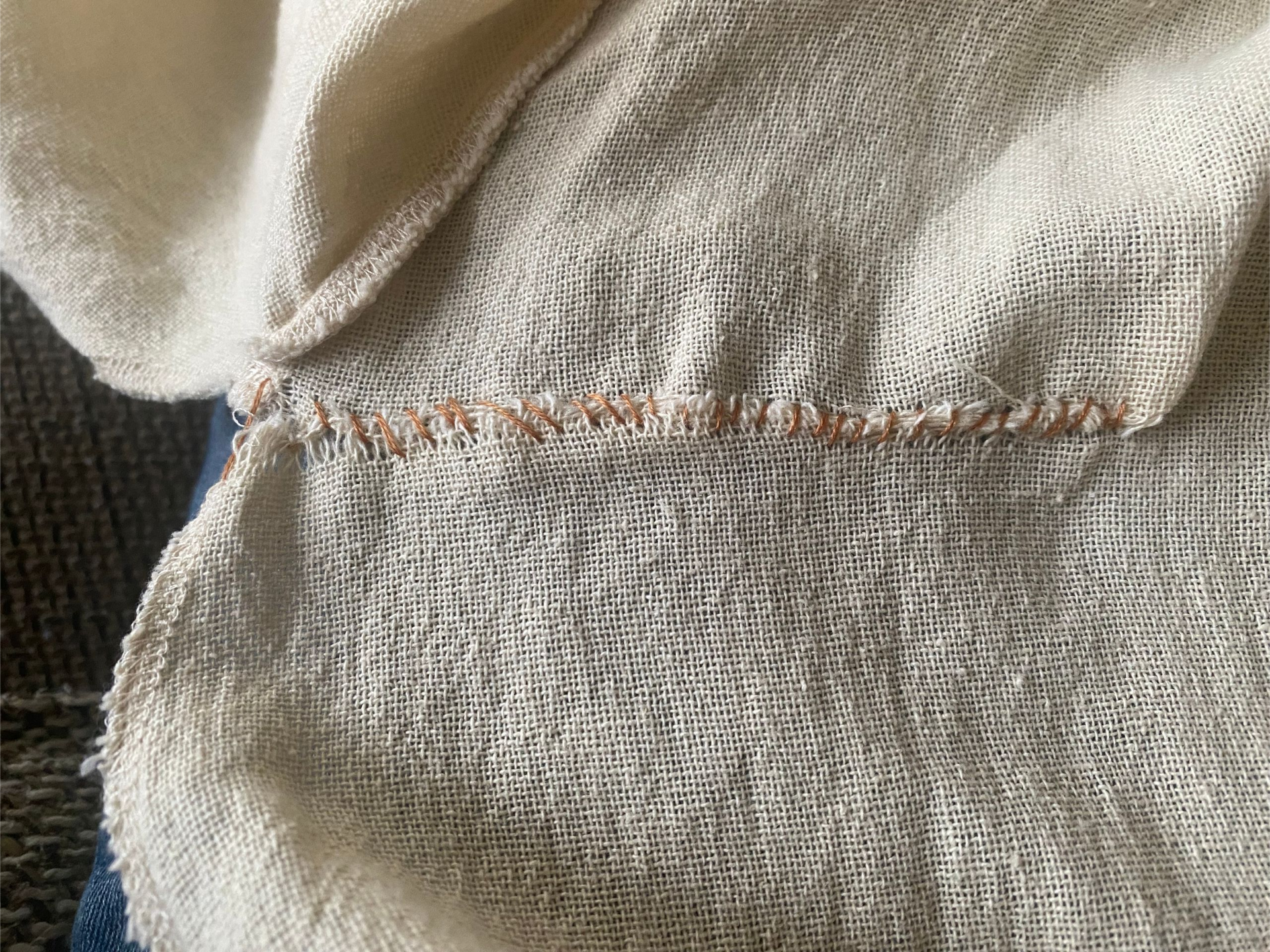 Detailopname van beige geweven stof, aan elkaar genaaid met bruin garen.