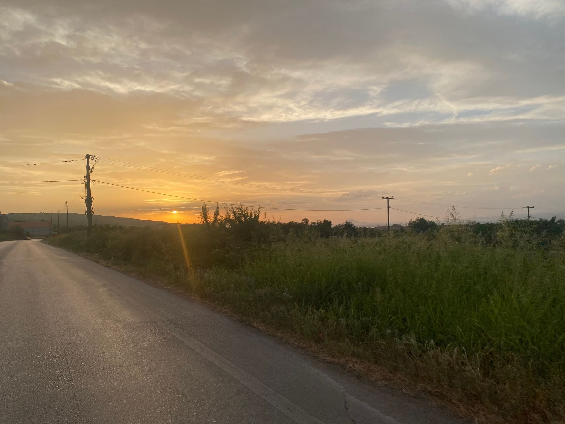 Zonsondergang boven een landweg met groene velden. Vogels zitten op elektriciteitskabels.
