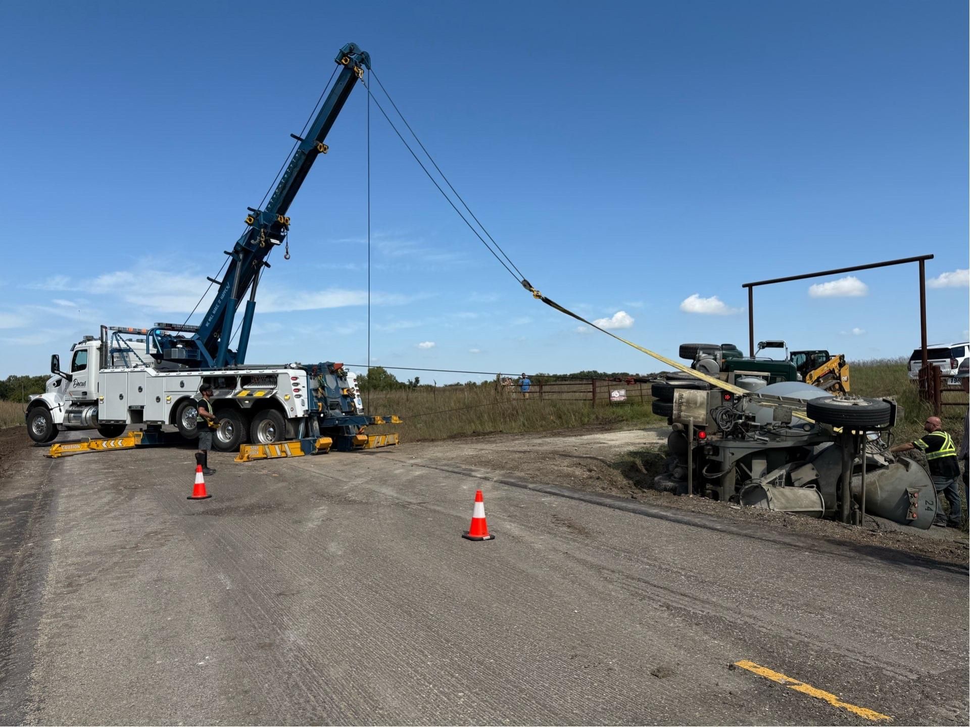 Tow truck lifting a heavy vehicle on a gravel road, with traffic cones and a clear blue sky