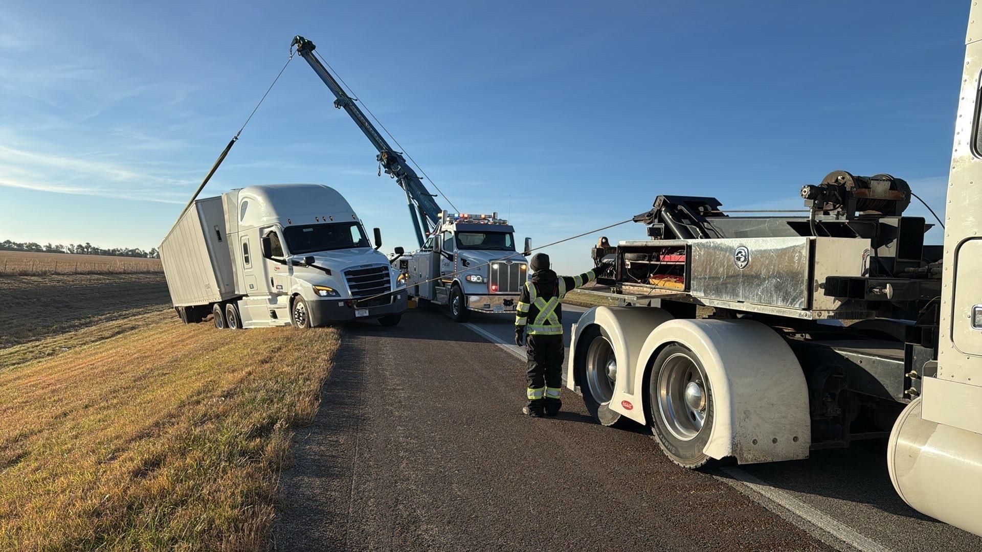 Tow truck crew clearing a crashed semi on a rural roadside at dusk