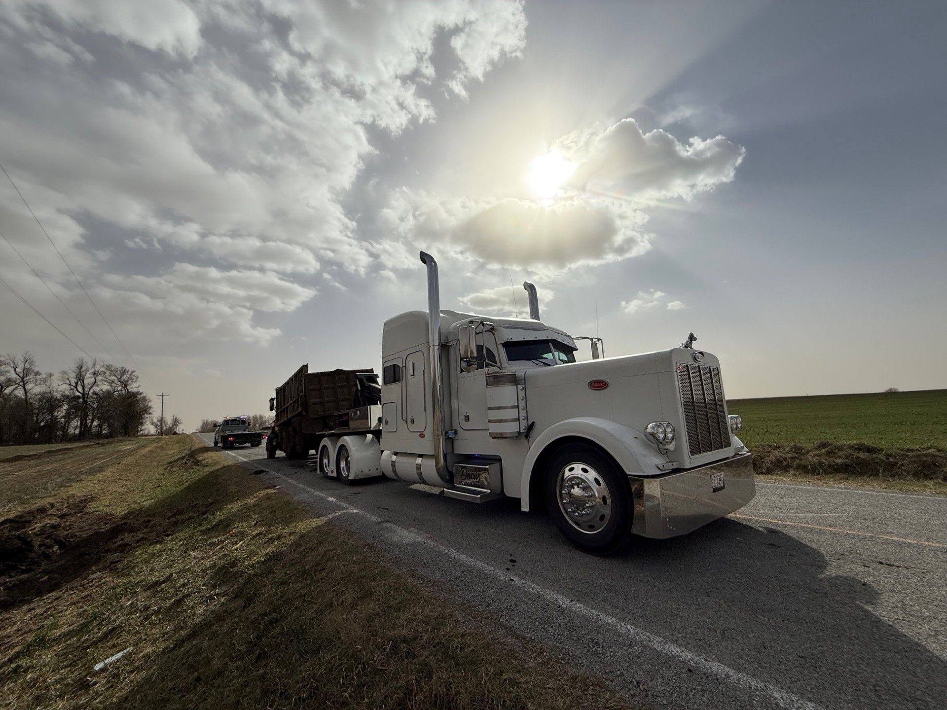 White semi-truck on a rural road under a bright cloudy sky