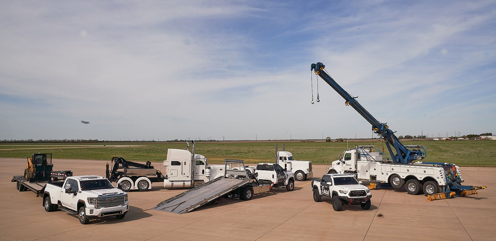 Line of white utility trucks and equipment at a flat roadside worksite under a cloudy sky