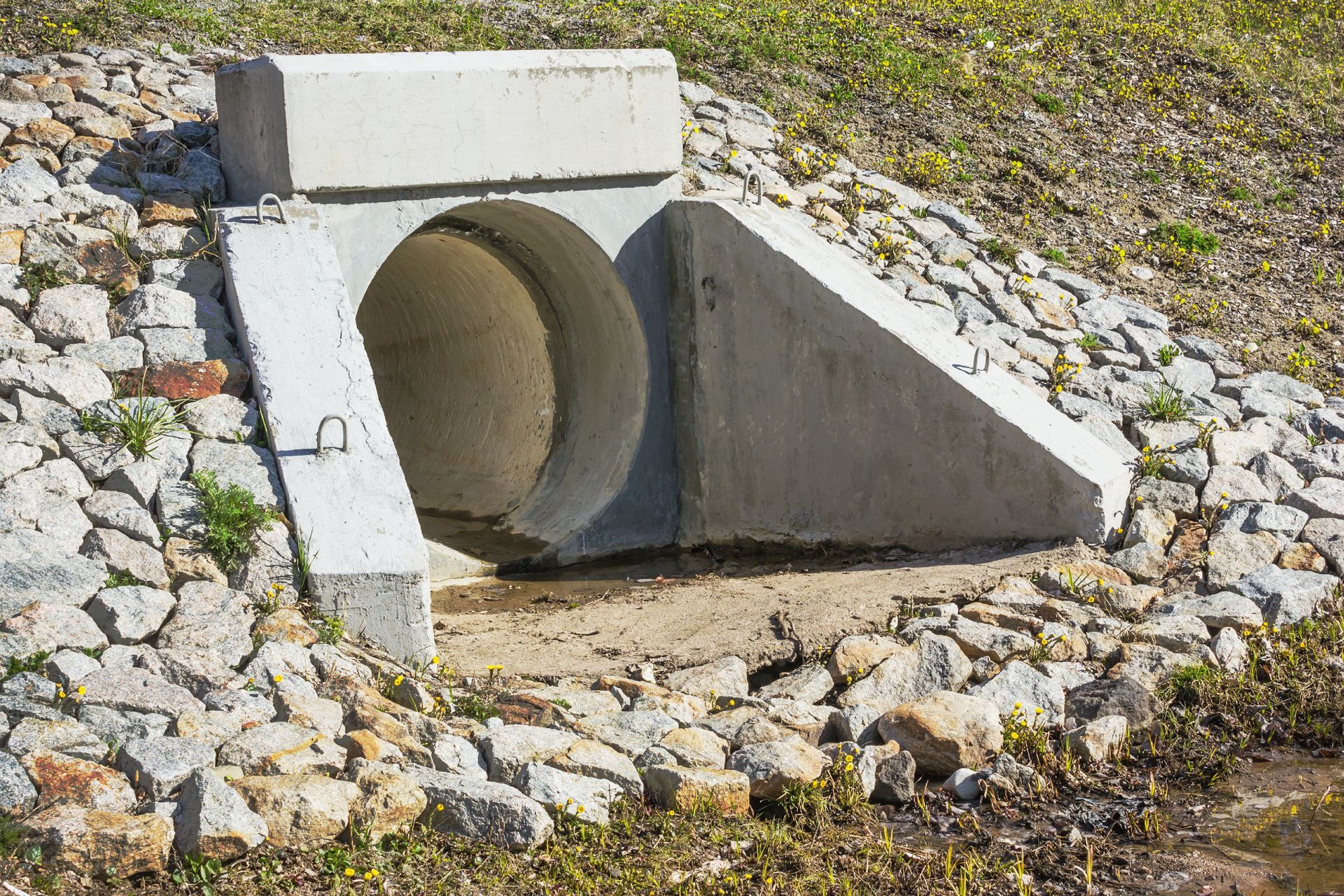 A series of cylindrical concrete utility structures partially buried in a dirt construction trench.