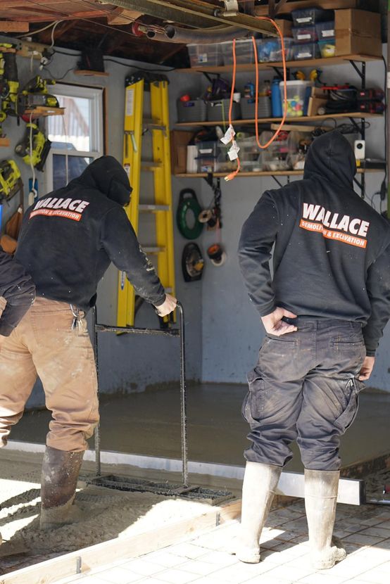 Two workers in hoodies leveling concrete in a garage.